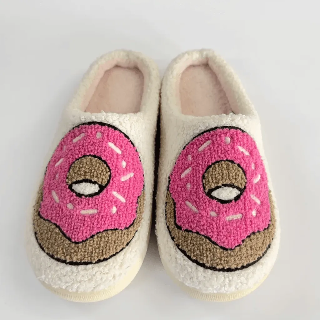Pair of cream plush slippers with pink and brown donut designs, shown from above to display motif placement and outlines