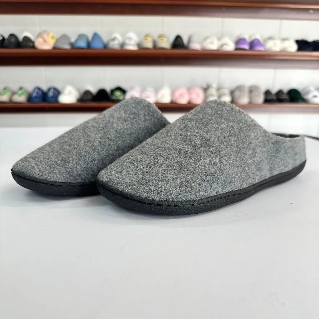 Grey closed-toe indoor slippers with black outsoles, showing the upper-to-outsole connection along the toe and sides